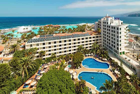 Hotellkompleks med bassenger og grøntområde nær havet. (AI-generert tekst)