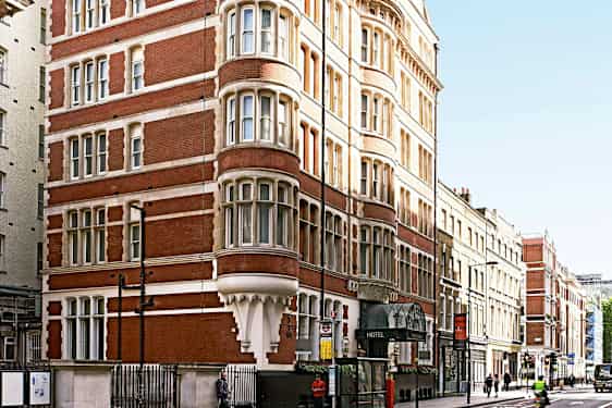 Et bilde av en rød murbygning med mange vinduer og et hotell i første etasje. (AI-generert tekst)