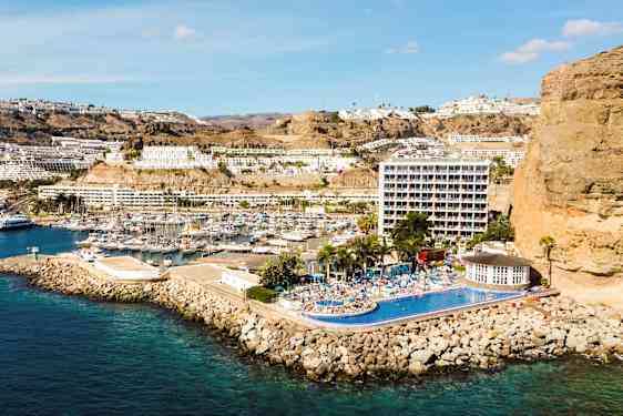 Bilde av en kystby med marina, bygninger i en skråning og hotell med basseng. (AI-generert tekst)