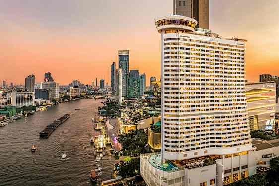 Utsikt over en elv omgitt av høye bygninger under en solnedgang. Et stort hotell er synlig i forgrunnen. (AI-generert tekst)