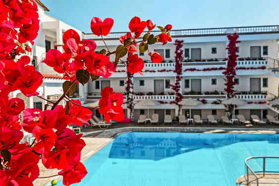 Blomstrende røde klatreplanter ved en bygning med et basseng foran. (AI-generert tekst)