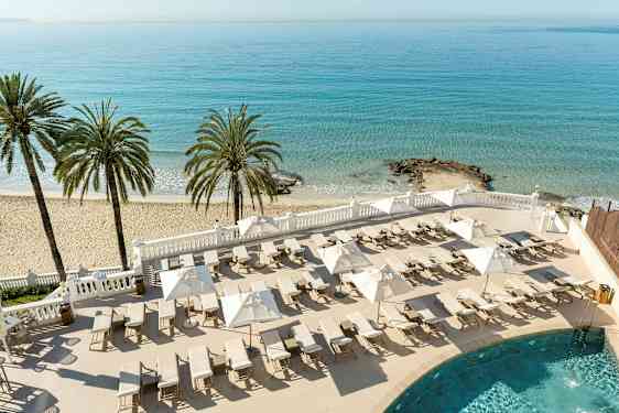 En strand med palmer, solsenger og parasoller ved et blått hav. (AI-generert tekst)