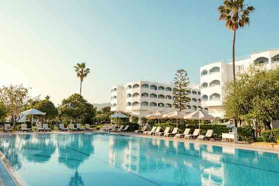 Hotellbygning med basseng, solsenger og parasoller i forgrunnen. (AI-generert tekst)