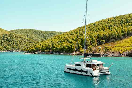 Seilbåt som ligger forankret ved en kyst med grønne åser. (AI-generert tekst)