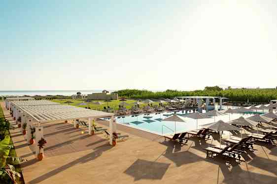 Et utendørs svømmebasseng med solsenger og parasoller på et hotellområde nær havet. (AI-generert tekst)