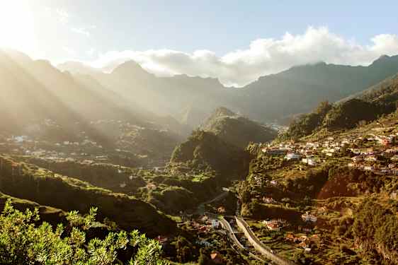 Utsikt over en grønn dal med hus og fjell i bakgrunnen på en solrik dag. (AI-generert tekst)