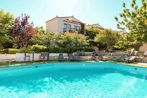 Et basseng omgitt av solsenger og et hus med balkonger i bakgrunnen. (AI-generert tekst)