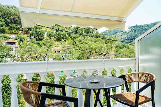 Utsikt fra en balkong med et lite rundt bord og to stoler, omgitt av grøntområder og et kupert landskap. (AI-generert tekst)