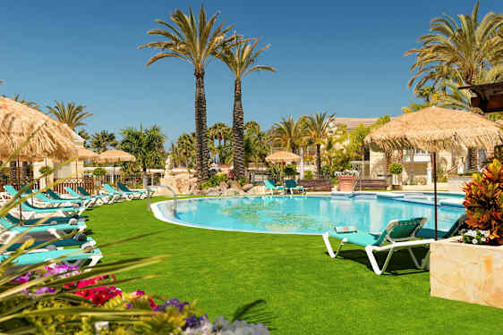 Et basseng omgitt av solsenger, parasoller og palmer på en solrik dag. (AI-generert tekst)