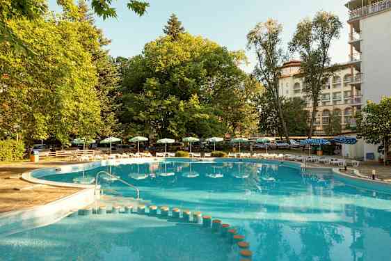 Et utendørs svømmebasseng med omkringliggende grønne områder og solsenger. (AI-generert tekst)