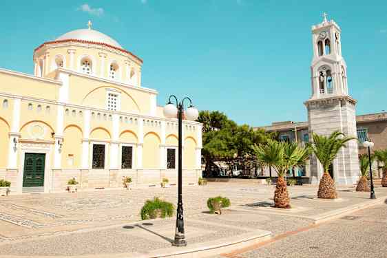 En gul bygning med kuppel og et klokketårn samt palmer og gatebelysning. (AI-generert tekst)