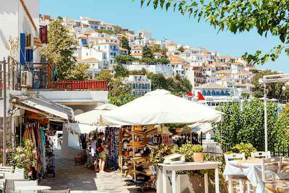 En pittoresk by med hvite hus med rødt tak på en skråning, parasoller og salgsboder i forgrunnen. (AI-generert tekst)