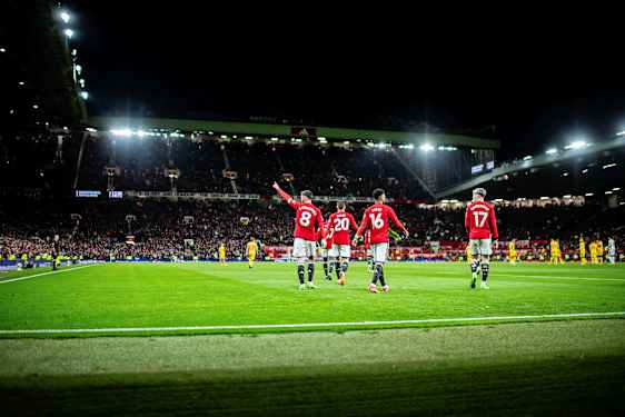 Fotballspillere i røde drakter på en opplyst fotballarena under en kveldskamp. (AI-generert tekst)