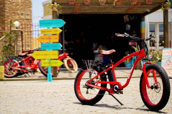 Rød sykkel på brosteinsunderlag med fargerike veiskilt i bakgrunnen. (AI-generert tekst)