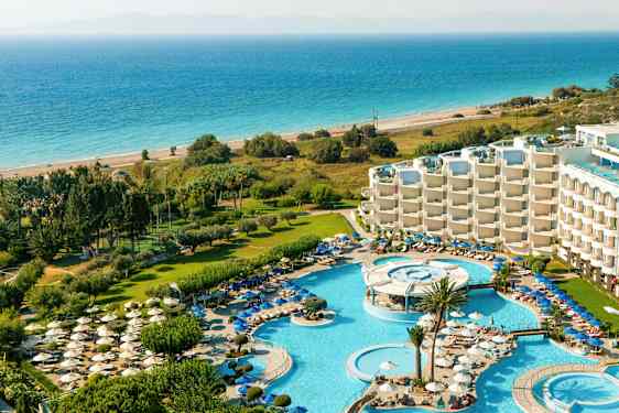 Utsikt over en resort med bassengområder, solsenger, grøntområder og havet i bakgrunnen. (AI-generert tekst)