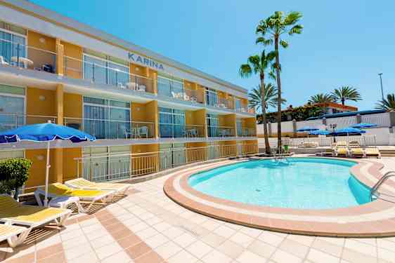 Et utendørs svømmebasseng med solsenger nær en leilighetsbygning og palmer. (AI-generert tekst)