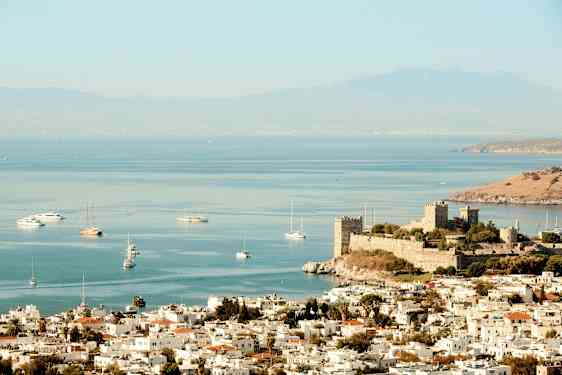 Bilde av en by ved havet med en gammel borg nær kysten og båter på vannet. (AI-generert tekst)