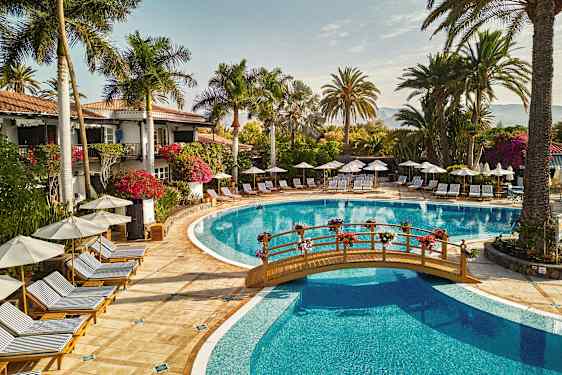 Utendørs bassengområde med solsenger, parasoller og omkringliggende palmer. (AI-generert tekst)