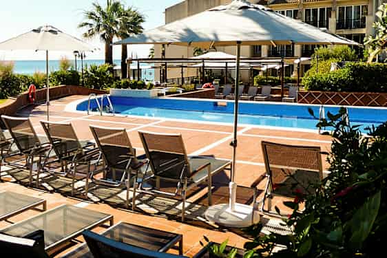 Et utendørsbasseng med solsenger og parasoller. (AI-generert tekst)