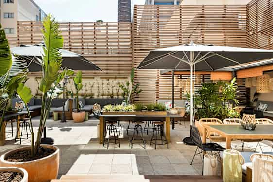 En utendørs terrasse med bord, stoler og plantepynt, omgitt av trepaneler. (AI-generert tekst)