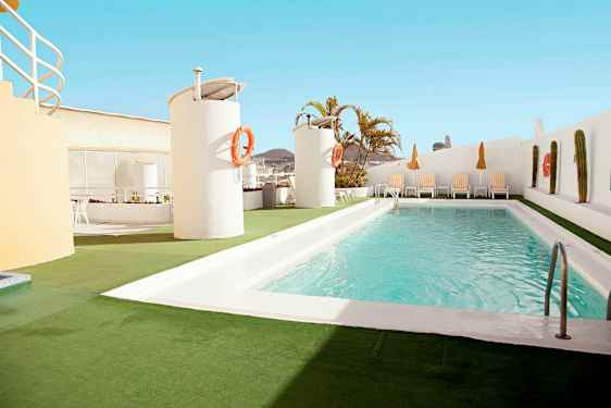 Et utendørs basseng ligger på en takterrasse med solsenger og parasoller rundt. (AI-generert tekst)