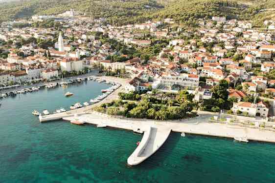Luftfoto av en kystby med båter i en havn og hus med røde tak. (AI-generert tekst)