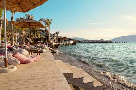 Solstoler og parasoller på en trebrygge ved vannet. (AI-generert tekst)