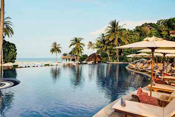 Et infinity-basseng omgitt av solsenger og parasoller med utsikt over den tropiske naturen og havet. (AI-generert tekst)