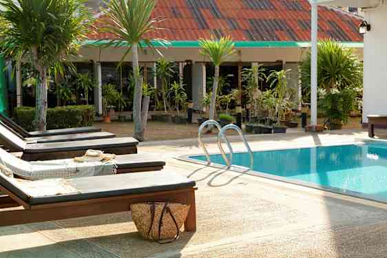 Solstoler ved et basseng med frodige trær og bygning i bakgrunnen. (AI-generert tekst)