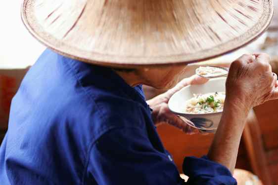 En person i blå klær og hatt spiser fra en bolle med en skje. (AI-generert tekst)