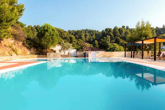 Utendørsbasseng omgitt av solsenger og parasoller med frodig bakgrunn. (AI-generert tekst)