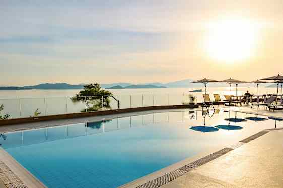 Et svømmebasseng med utsikt over havet og solnedgangen, parasoller og solsenger ved kanten. (AI-generert tekst)