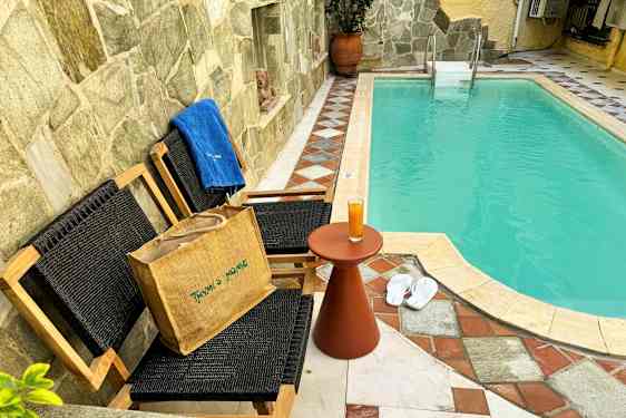 Et basseng med to stoler og et bord, samt tøfler og et håndkle ved siden av. (AI-generert tekst)