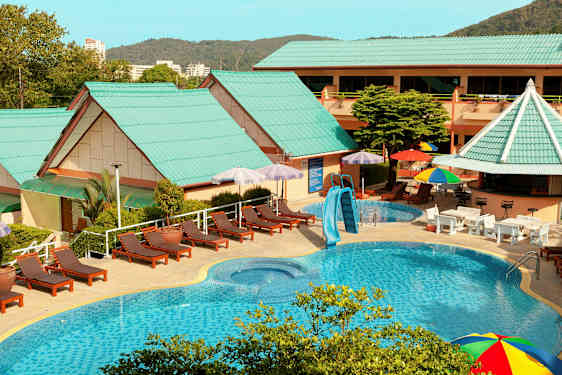 Utendørs bassengområde med solsenger, parasoller og bygninger med grønne tak. (AI-generert tekst)