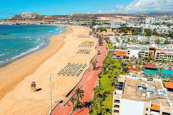 Strand med rekke av parasoller og hav i bakgrunnen. (AI-generert tekst)