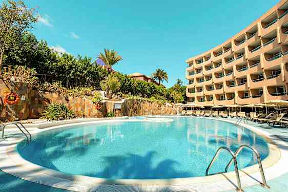 Bilde av et basseng med solsenger rundt og en fleretasjes hotellbygning i bakgrunnen. (AI-generert tekst)