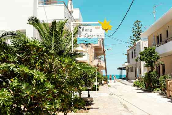 En solrik gate med grøntområder, bygninger og et skilt som viser 'Anna Katerina'. (AI-generert tekst)