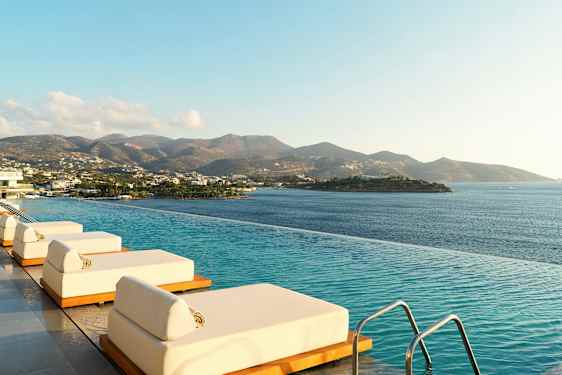 Infinitybasseng med solsenger ved havet med fjell i bakgrunnen. (AI-generert tekst)