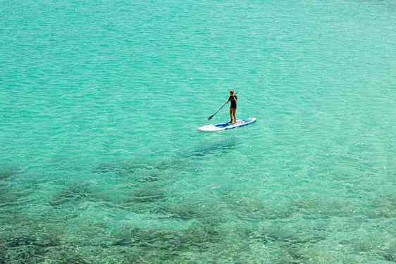 Person som padler stående på en paddleboard i klart turkis vann. (AI-generert tekst)