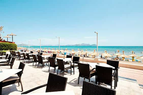 Uteservering med utsikt mot en sandstrand og havet med parasoller. (AI-generert tekst)