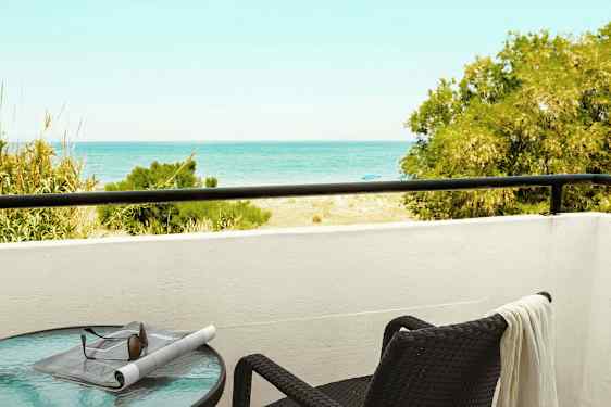 En balkong med utsikt mot havet, et bord med solbriller og en avis samt en stol med et håndkle. (AI-generert tekst)