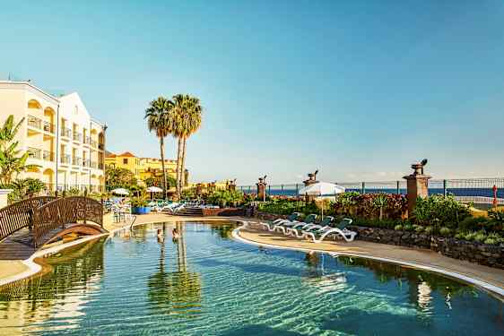 Hotell med basseng, solsenger og palmer ved kysten. (AI-generert tekst)