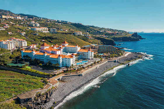 Et hotell med røde tegltak ved sjøen, omgitt av grønne åser. (AI-generert tekst)