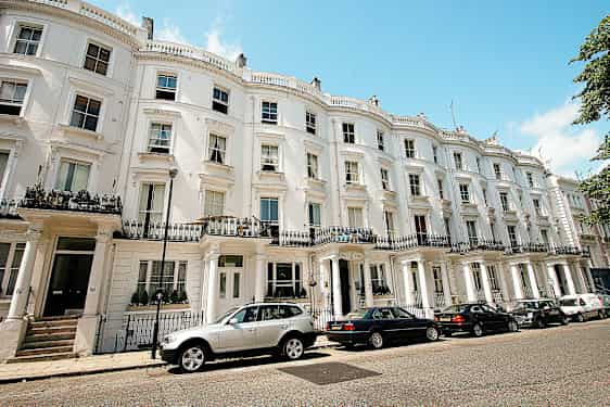 En husrekke med hvite fasader og parkerte biler foran. (AI-generert tekst)