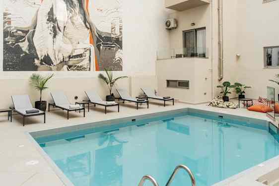 Bilde av et utendørs svømmebasseng ved et hotell med solsenger og et stort kunstverk på veggen. (AI-generert tekst)