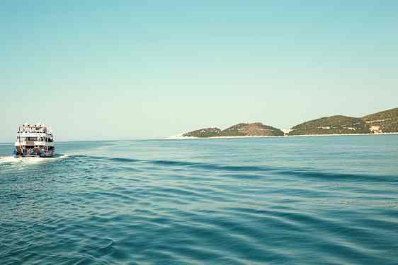 En båt kjører over et rolig hav med noen lave øyer i horisonten. (AI-generert tekst)