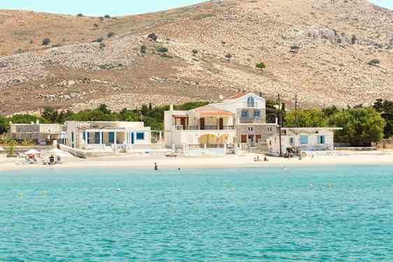 Bilde av en klarblå bukt med en sandstrand som har hus og åser i bakgrunnen. (AI-generert tekst)