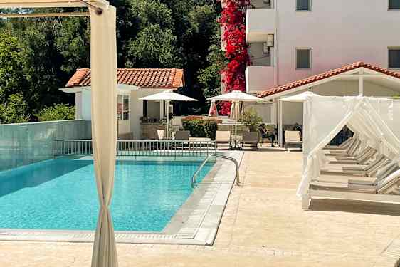 Et utendørsbasseng med solsenger og et hvitkalket hus i bakgrunnen. (AI-generert tekst)