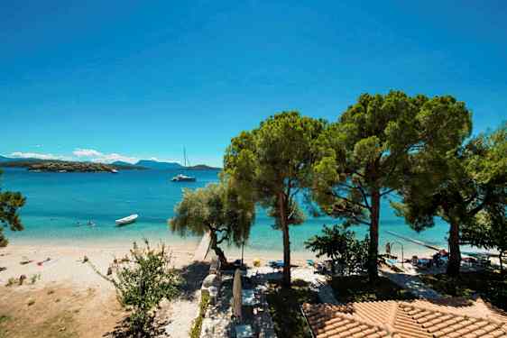 Utsikt over en sandstrand ved et blått hav med noen trær og strandparasoller. (AI-generert tekst)