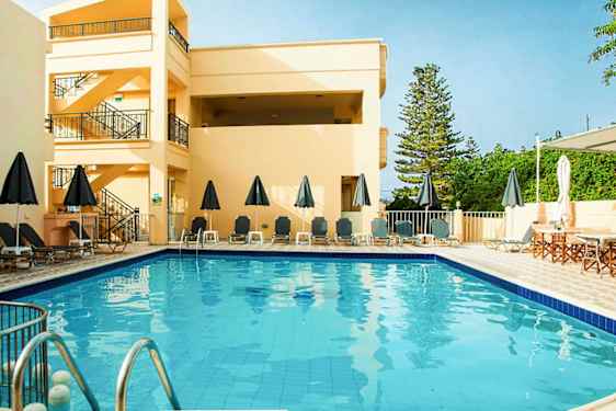 Utendørsbasseng med solsenger og parasoller, omgitt av bygninger og grøntområder. (AI-generert tekst)